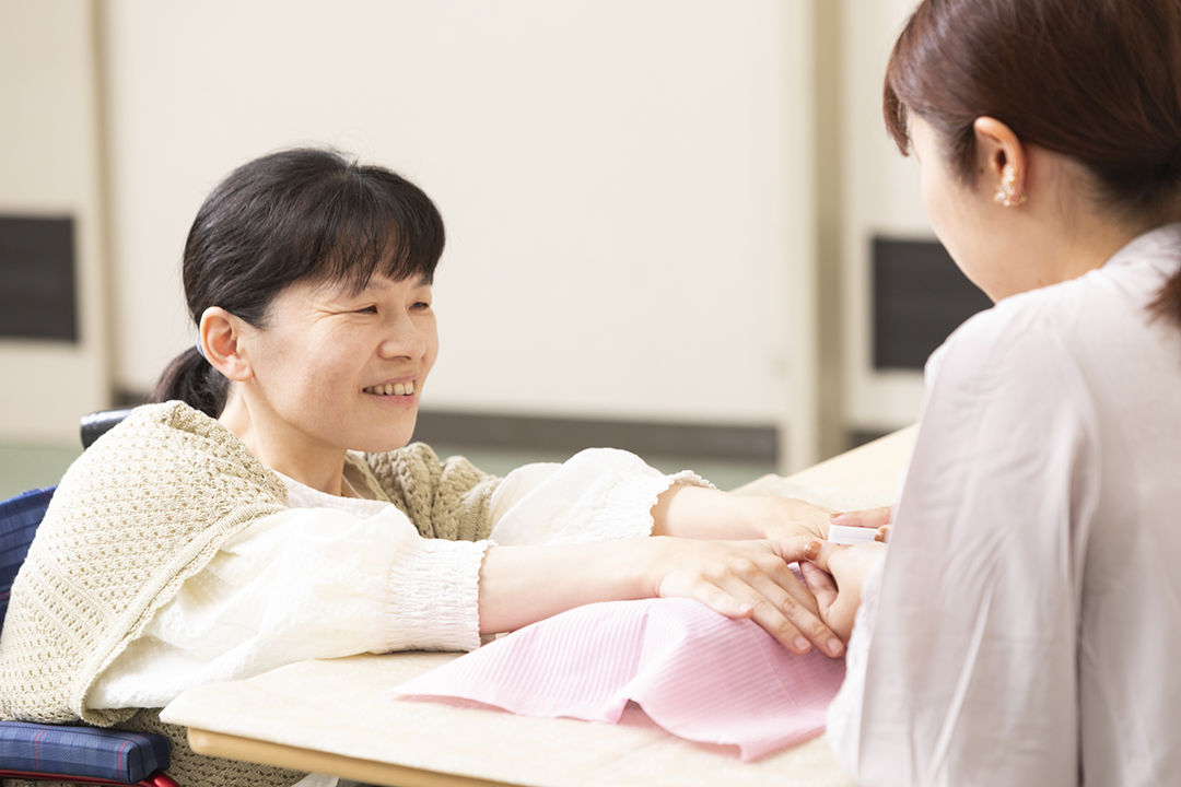 20年ぶりにネイルを体験して微笑んでいる油利さん左側と施術をしてくれている荒金さん右側が向き合っているの写真