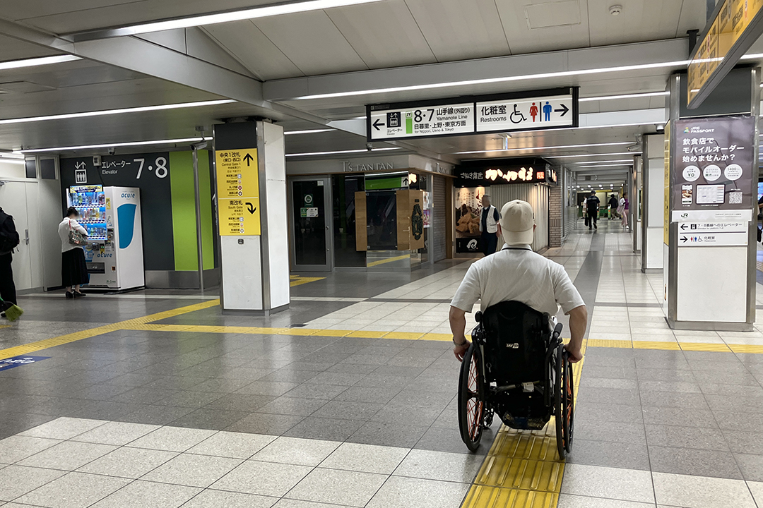 右方向にトイレがある看板を見ている車いすの筆者