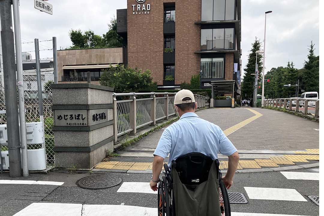 歩道を右方向に進む車いすの筆者の写真