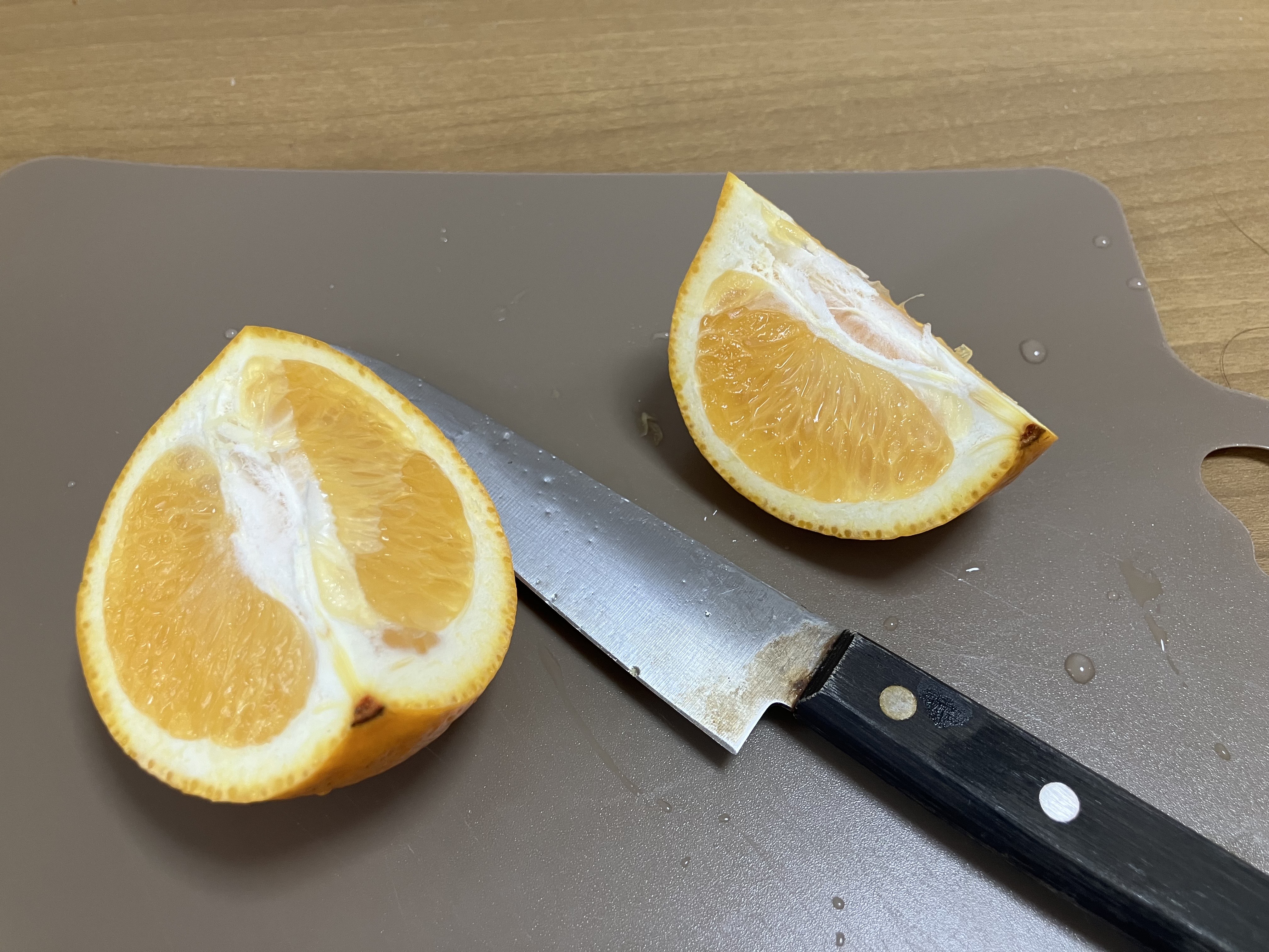 茶色のまな板の上に果物ナイフと4分の1に切られたオレンジが乗っている