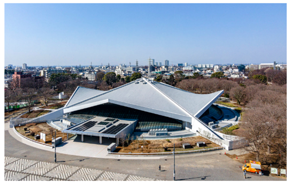 駒沢オリンピック公園総合運動場体育館を上から見た写真。周囲には木々が多く、自然と都市が調和して晴れた空の下で、全体的に明るく爽やかな雰囲気が伝わってきます
