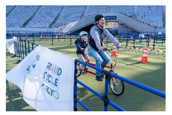 パラサイクリング体験の様子。スタジアムの中で2人乗りのタンデム自転車に乗っている参加者。周囲にはコーンや柵が設置され、安全に配慮されたコースで協力しながら走行を楽しんでます