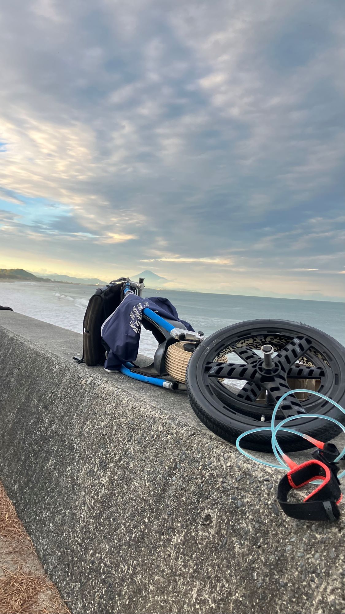 海岸の堤防の上に、分解した車いす、乗り換えて波に乗ってるんだなと感じる写真、曇天の奥に小さく富士山が見える 静波での一枚