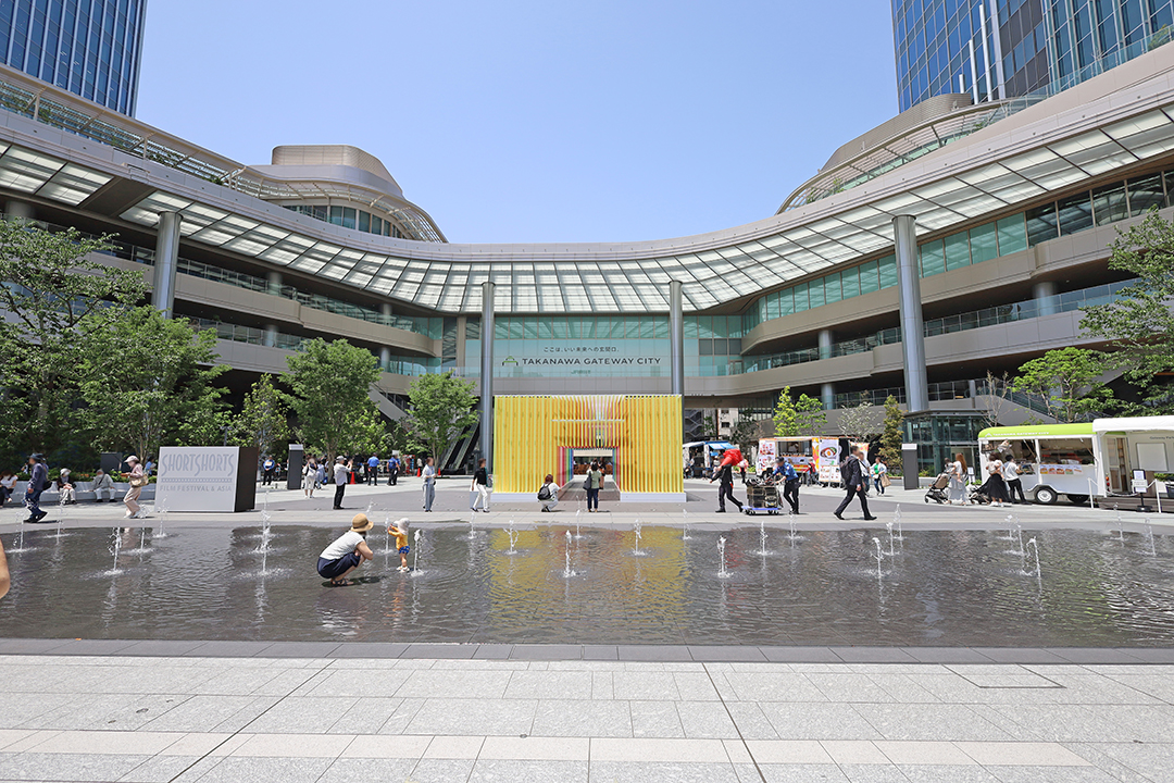 駅前広場の正面に小さな噴水がたくさんあり、水たまりができていて子供たちが遊んでいる