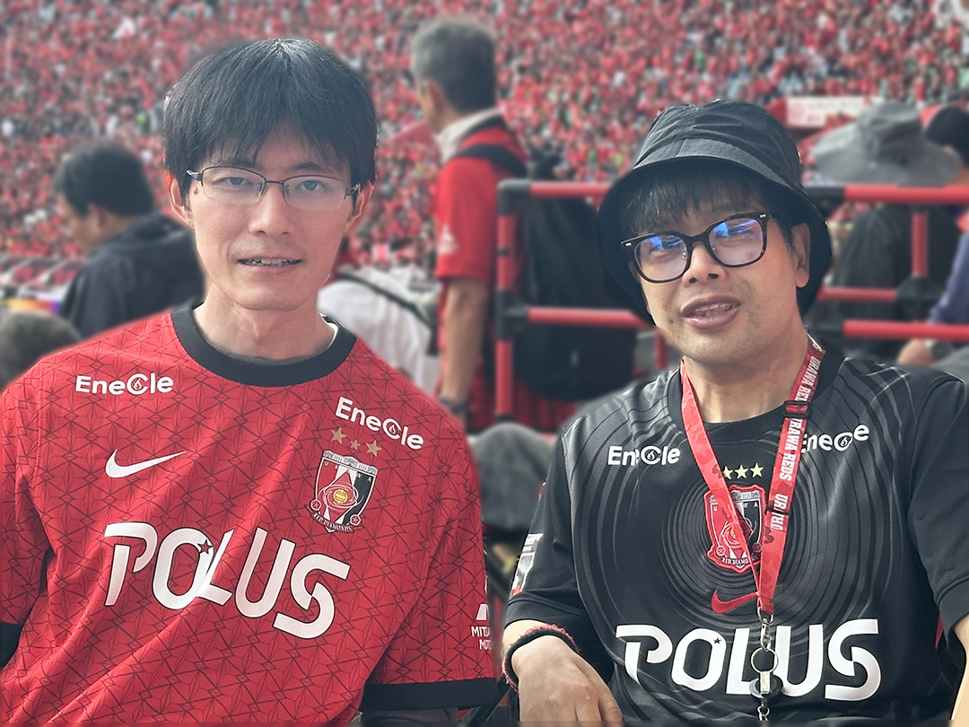 らくゆく編集スタッフＹと翔太のツーショット。車いす席から見た客席は赤いユニフォームを着た多くのサポーターで埋まり、一体感が感じられる。