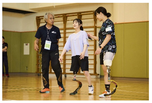体育館内で義足での歩き方を教えてもらっている女性二人