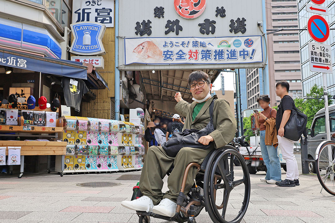 築地場外市場の入り口前で、周囲には観光客や買い物客が集まり、とても活気があり、楽しげです。