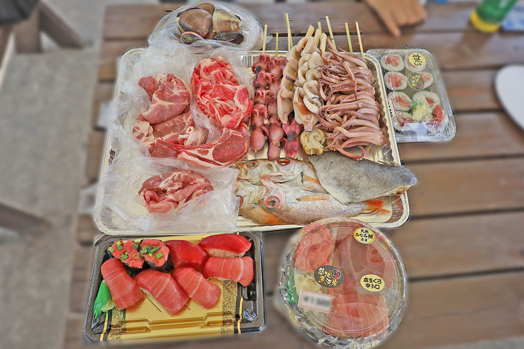 新鮮な魚介類や肉、寿司など豪華な食材が並び、これからバーベキューやパーティーが始まるワクワク感が感じられます。