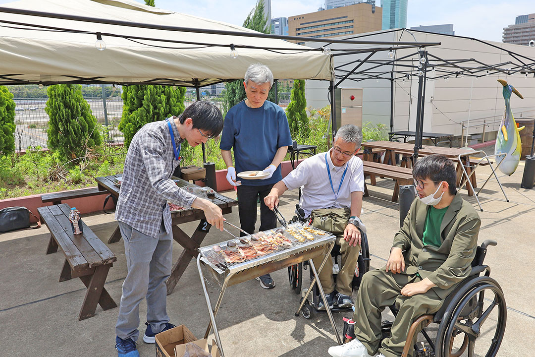 屋外でバーベキューを楽しんでいる様子が伝わり、みんなで協力して料理をしたり談笑したりしている姿が感じられます。