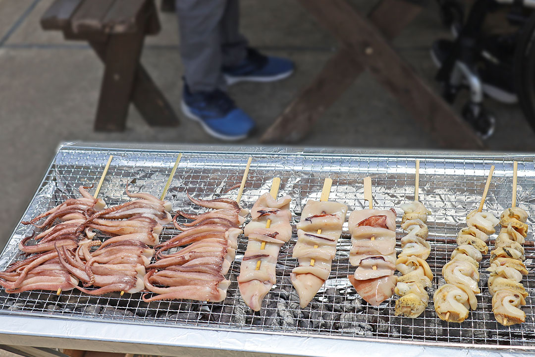 ゲソなどの串焼きが炭火の上で並んで焼かれており、香ばしい香りや焼き上がる音が感じられます。