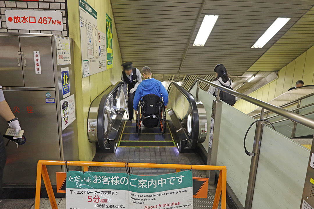 駅員に誘導されながら下りエスカレーターに乗る筆者