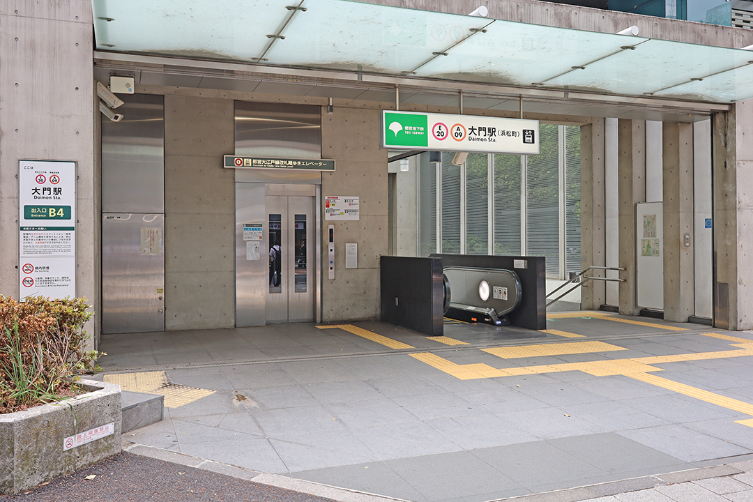 歩道の左側にある都営地下鉄大江戸線改札階行エレベーターとエスカレーターと階段
