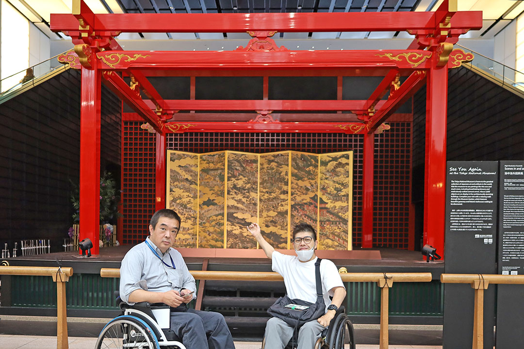 鮮やかな赤の伝統的な建築様式の舞台で、背景の金色の屏風も格式高い和の美しさが際立っています。 その前で車椅子の方が談笑しています。