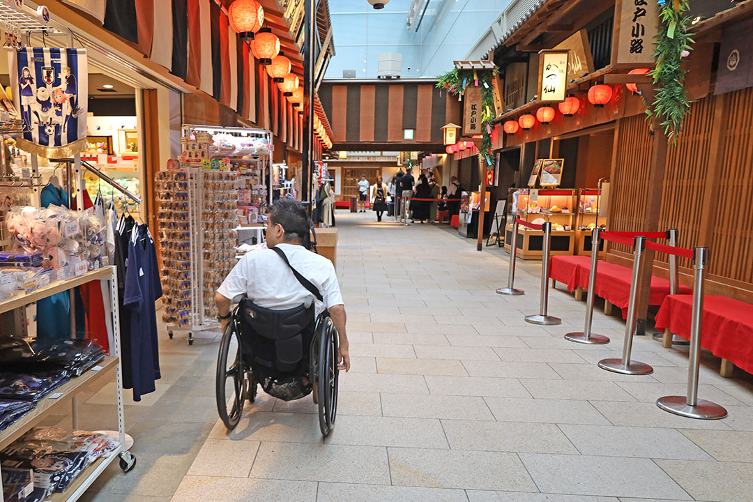 伝統的な日本の赤い提灯や木造の商店街を思わせる温かみと賑わいが感じられ、通路幅は広くお土産店や飲食店が並び、観光地らしい楽しい雰囲気も漂っています。