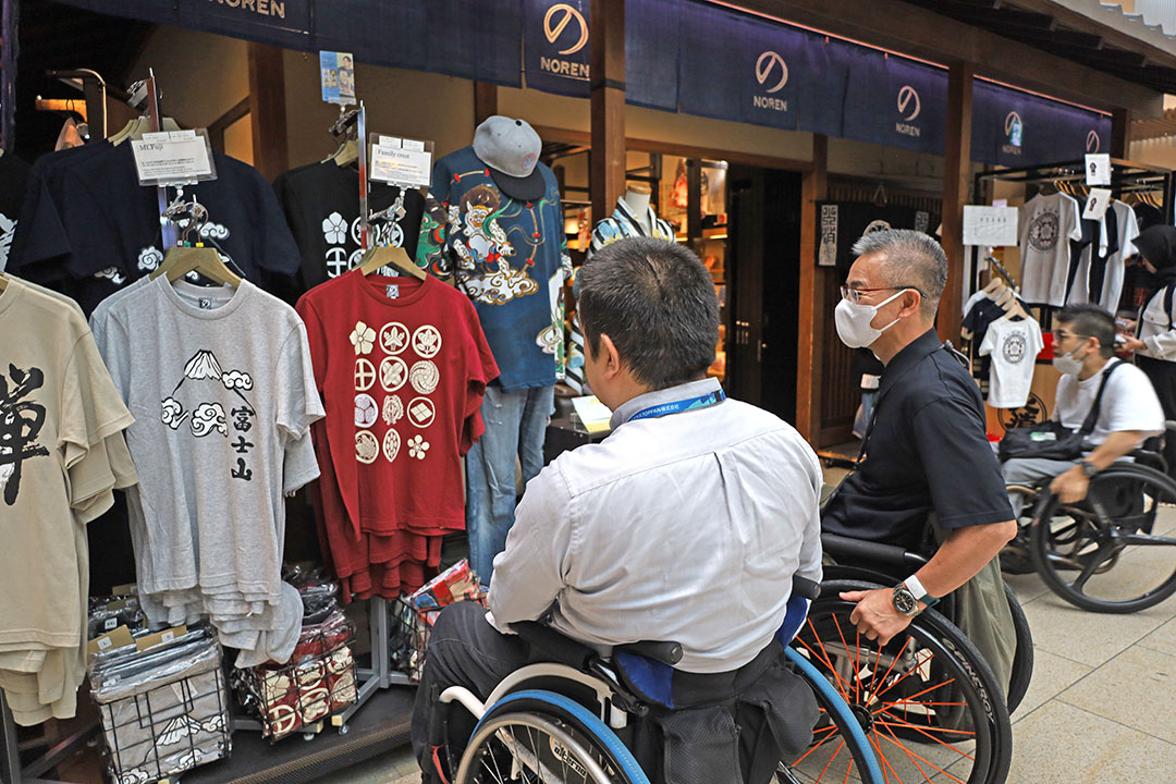 和風デザインのTシャツや雑貨が並ぶショップの前で、車椅子の方々が商品を楽しそうに見ている様子です。