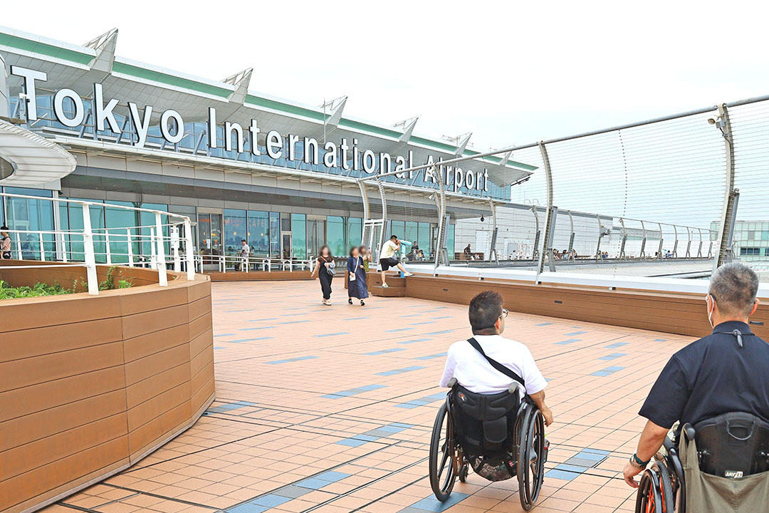 明るい屋外で、大きな「Tokyo International Airport」の看板が印象的で、非日常のワクワク感が伝わってきます。
