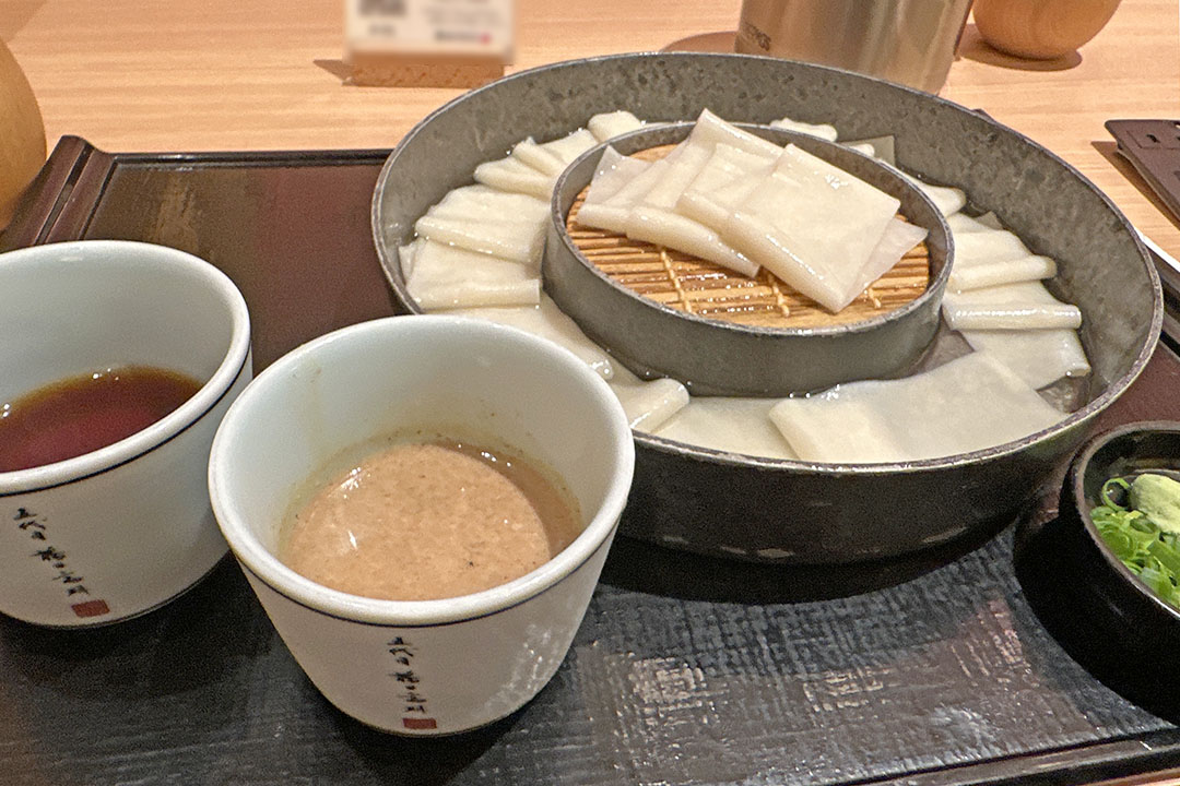 幅の広いうどんと、めんつゆ、ごまだれとねぎが添えられています。