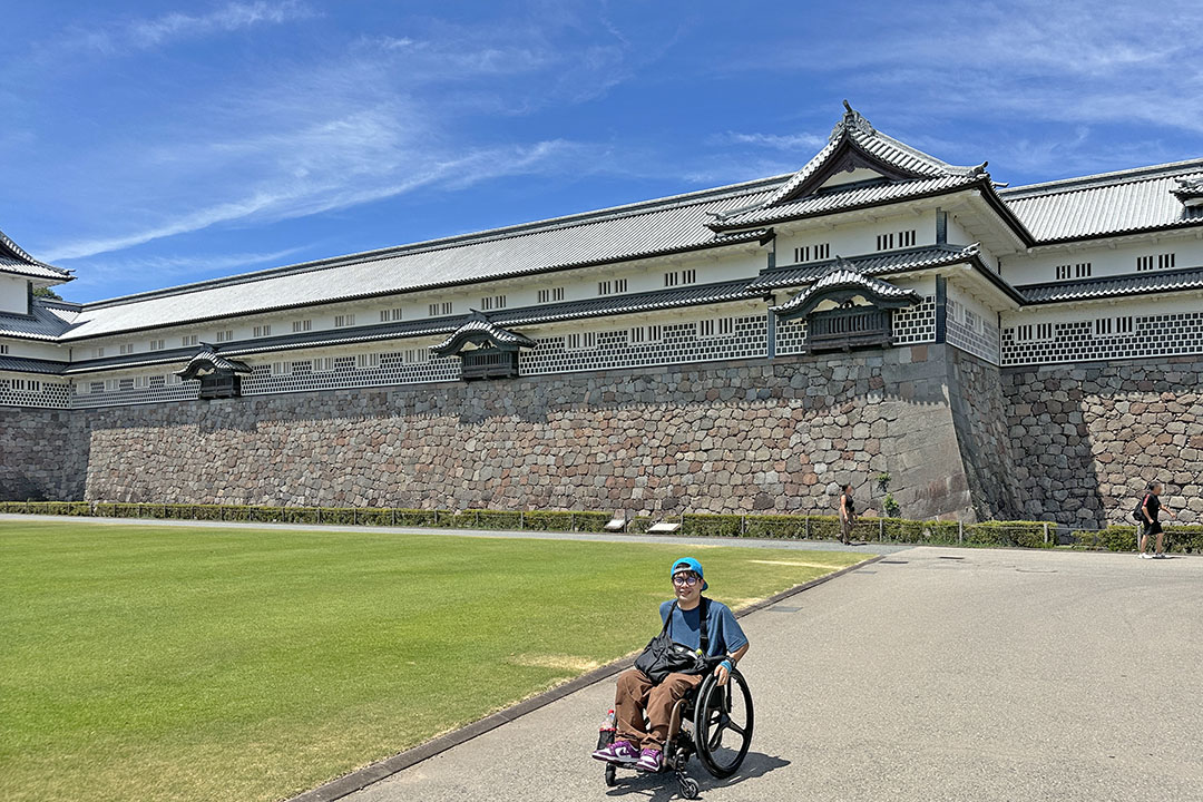 晴れ渡った青空の下、日本の伝統的な金沢城を背景に、歴史と自然に包まれた開放的で穏やかな雰囲気です。