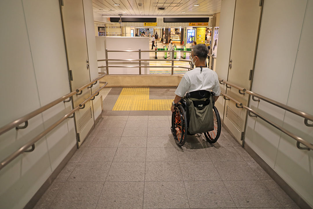 Eエレベーターを降りてスロープを下る車いすの男性