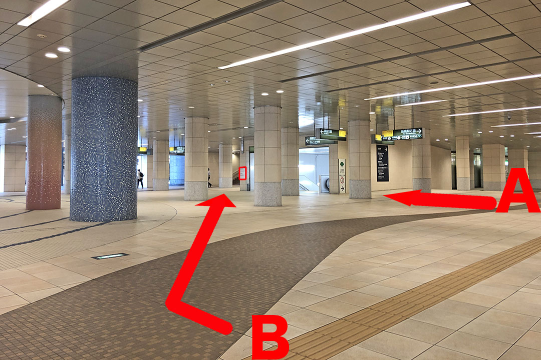 通路の斜め右前に大江戸線汐留駅への階段とエスカレーターが見える写真。