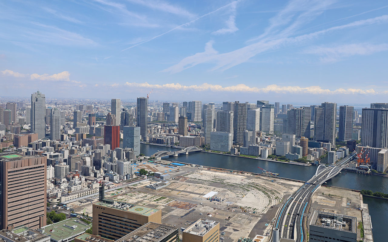 46階からの眺め。正面眼下は築地市場跡地とその先に墨田川が流れ、東京の街並みが見える写真。