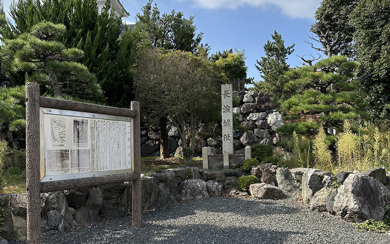 長浜城址の写真。松などの木々が植えられた区画に、当時の石垣が残っているのが見える。左には解説が書かれていると思われる看板が立っている