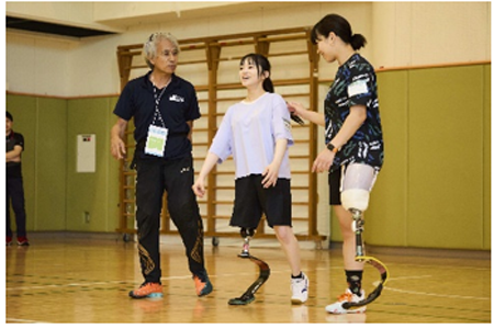 体育館内で義足での歩き方を教えてもらっている女性二人