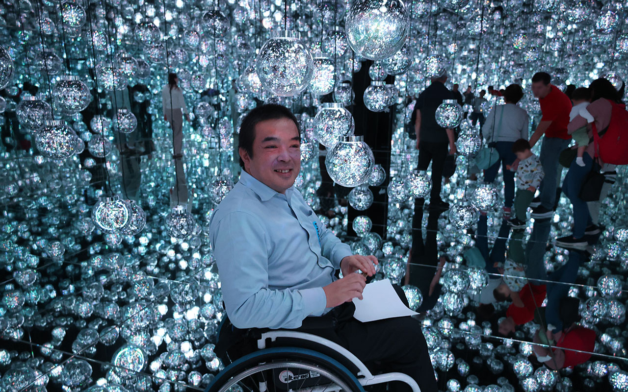 多数の光の球体(バブル)で埋め尽くされた空間の中で笑顔の車いすの男性