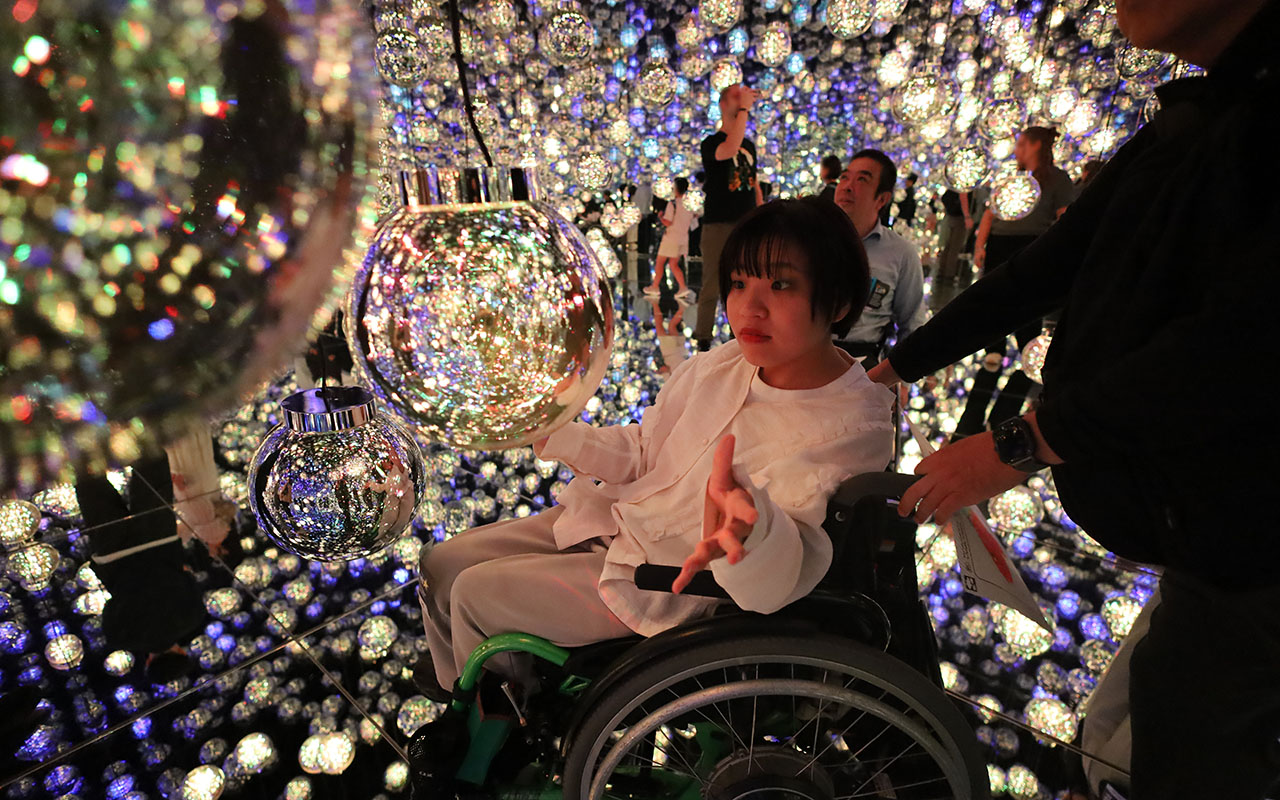 光の球体(バブル)に手を近づける車いすの女性