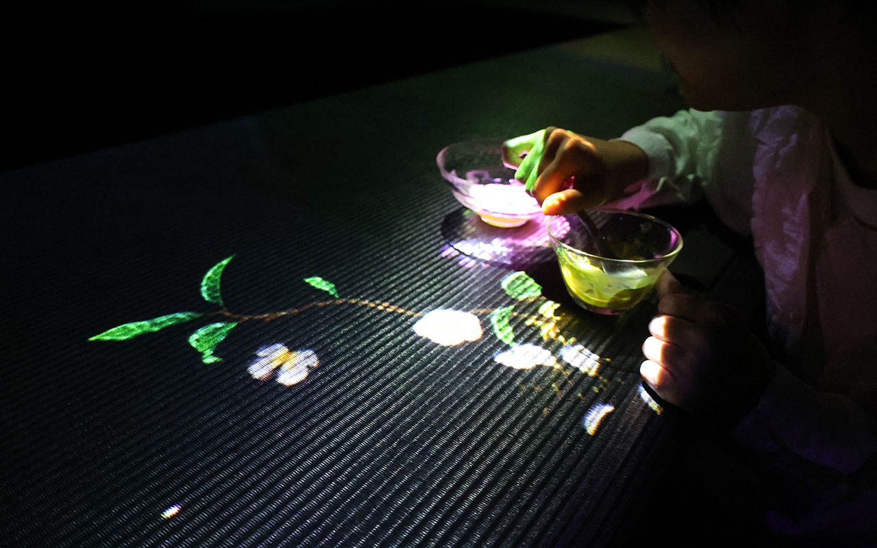 テーブルの右側は抹茶を飲み切ったグラスの中の花が枯れ始めた映像が映し出され、左側には抹茶のアイス入りのグラスから茶の木の映像が生えてきている