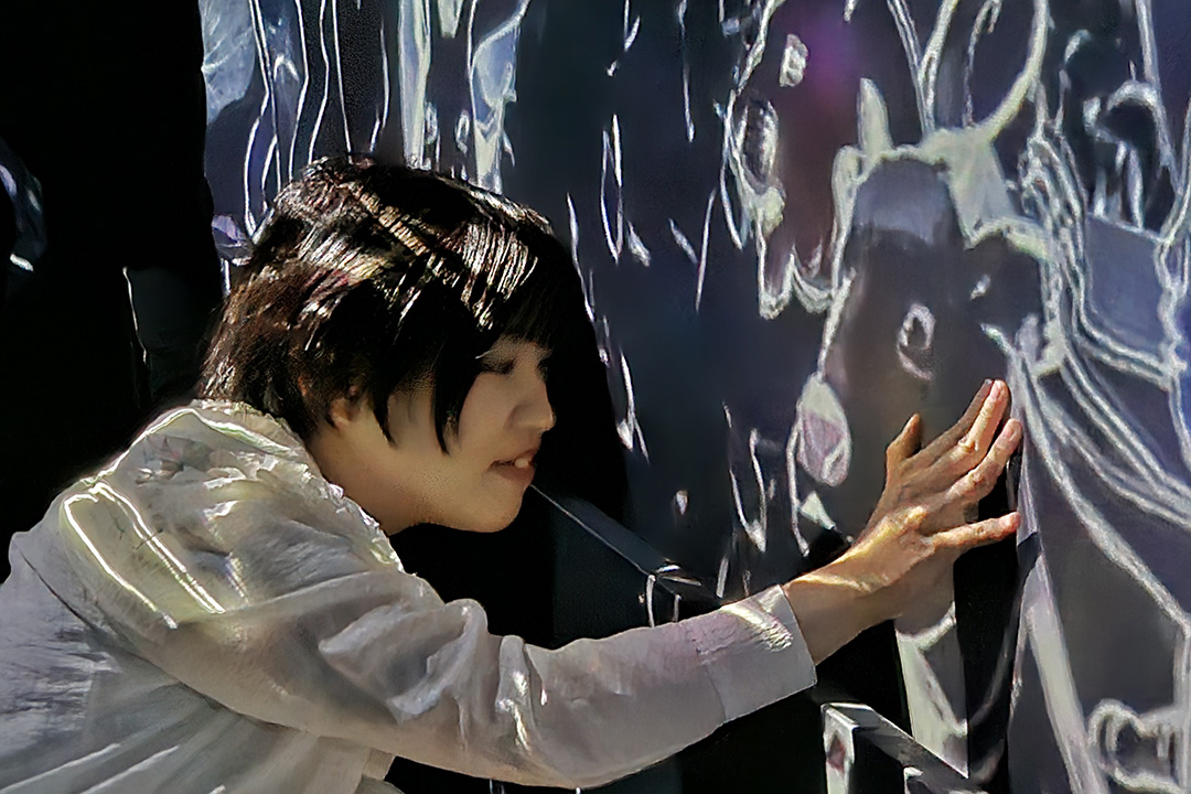 壁に映し出される牛のような動物の顔に手を付いている車いすの女性