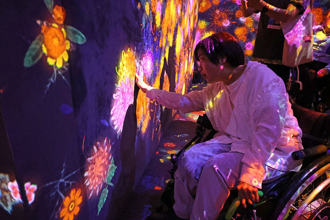 花が咲き乱れる映像の壁に手を付いている車いすの女性
