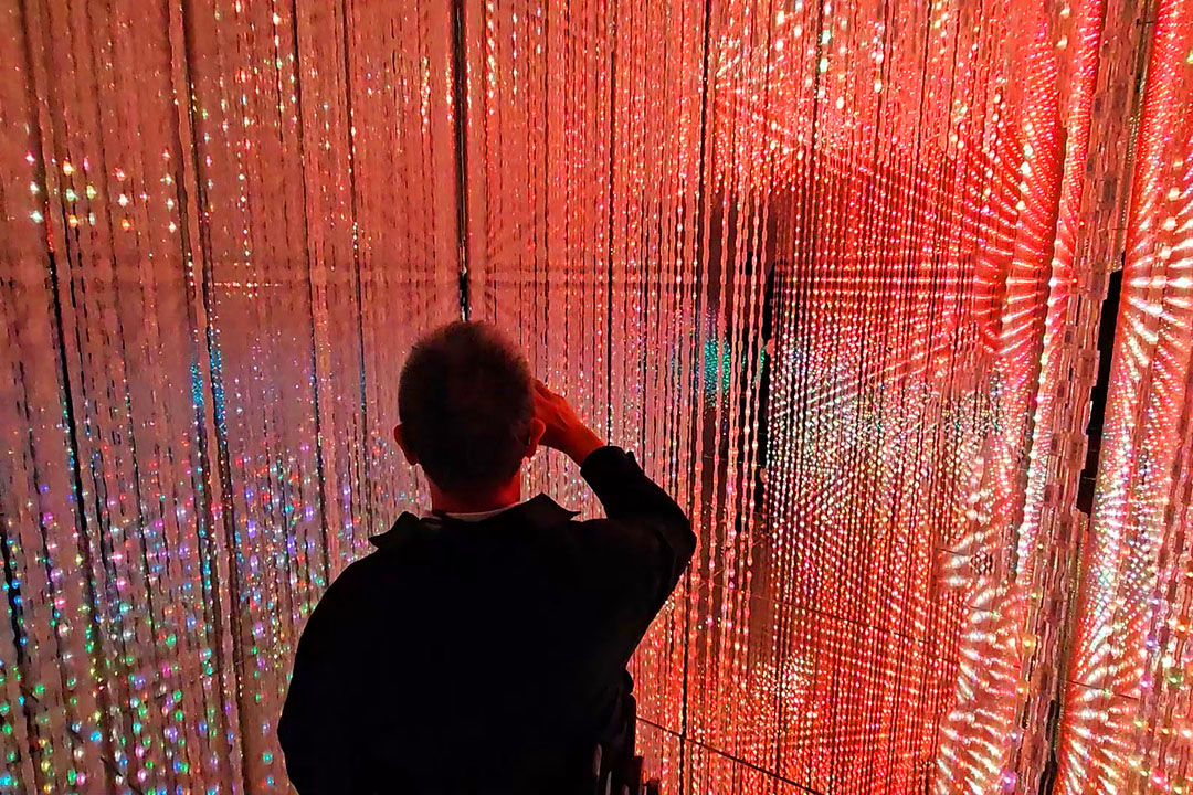 無数の赤系の光の点によって構成された映像の前にいる車いすの男性
