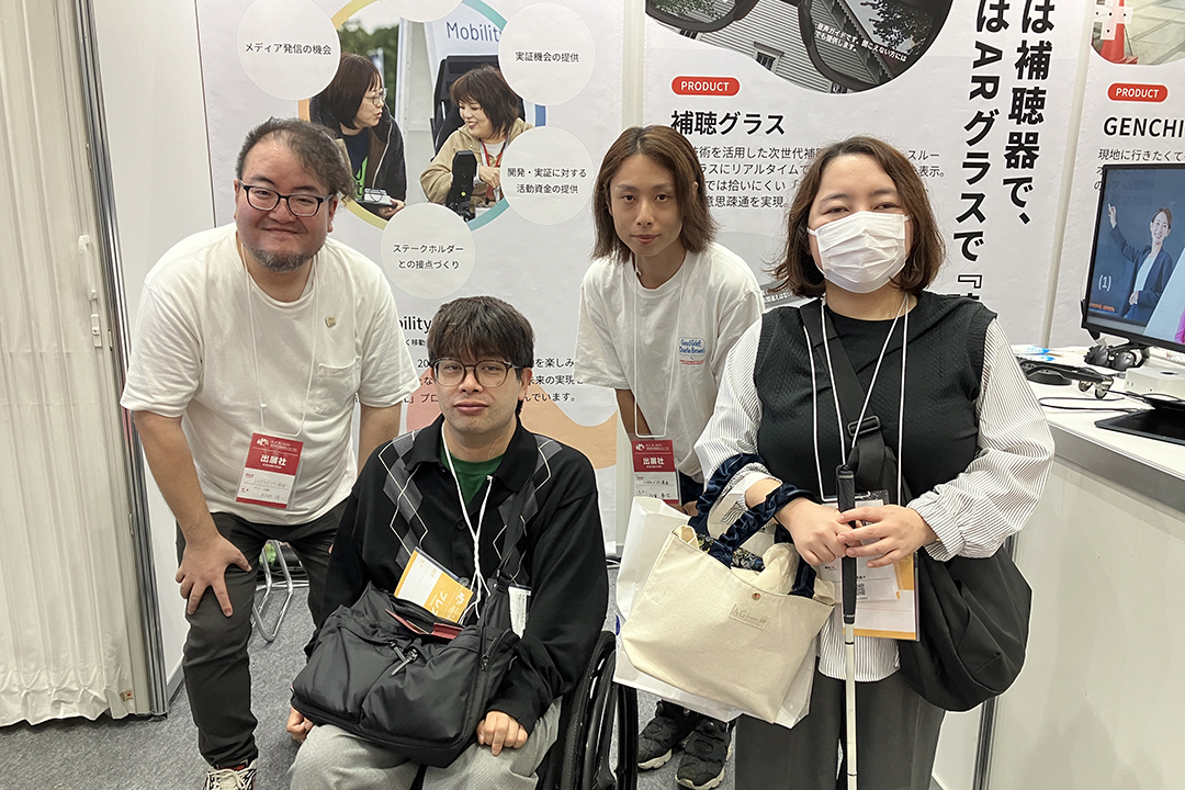 トヨタ・モビリティ基金ブースの前でスタッフ2人とらくゆくスタッフ2人で撮影