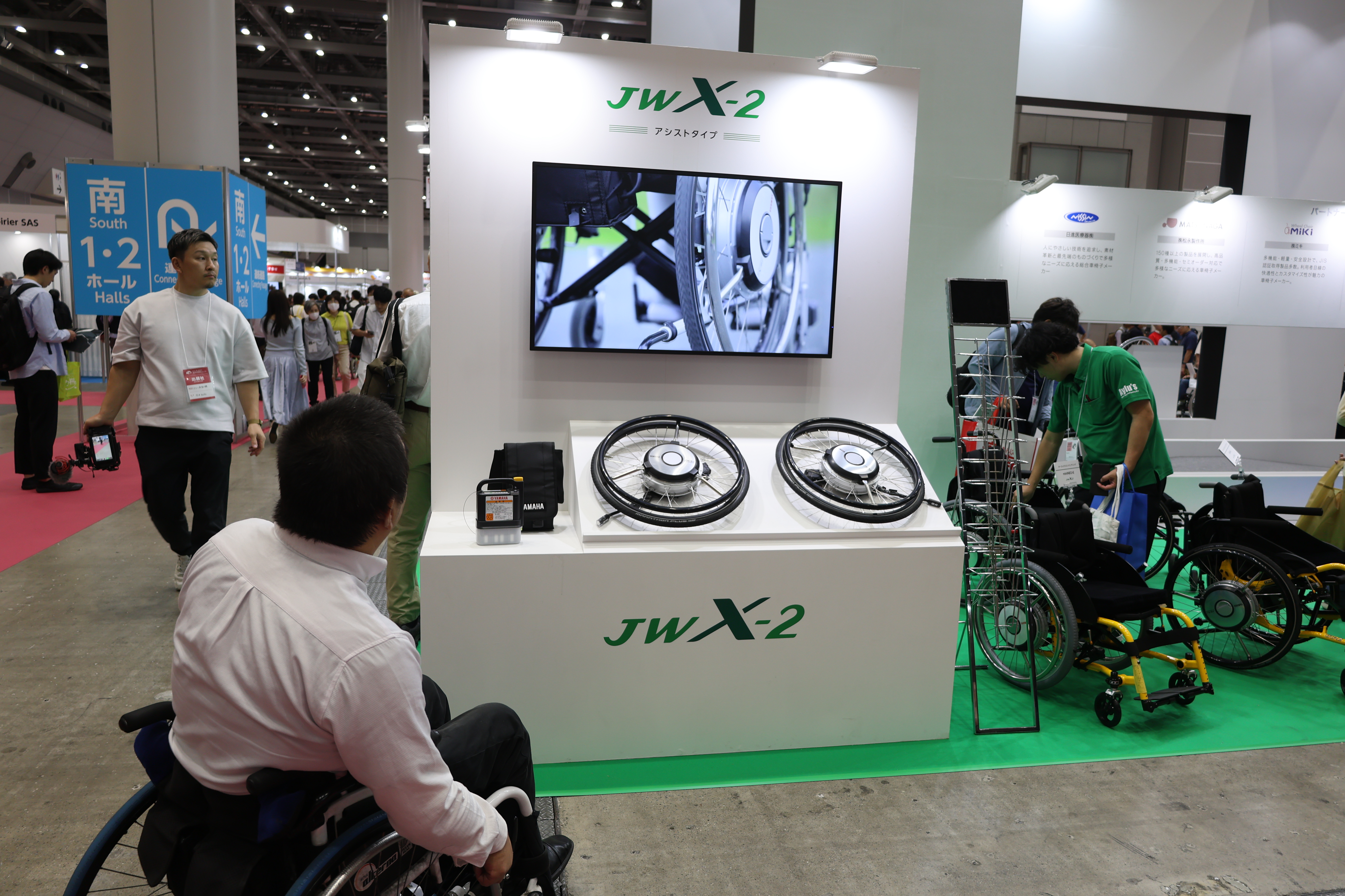 車いす電動アシストユニットの部品が陳列した上に宣伝用モニター