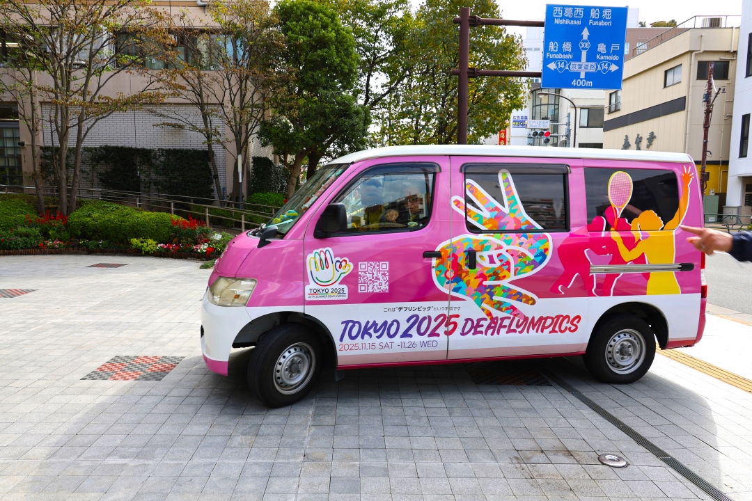 桜色にラッピングされたキャラバンカーが東京に入ります。デフリンピックの手話がデザインされています