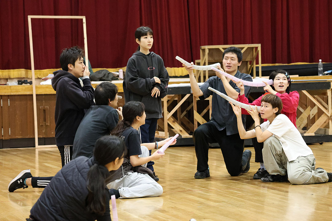 しゃべっている声をラッパのようなもので聞いている人たちの演技をする役者たち