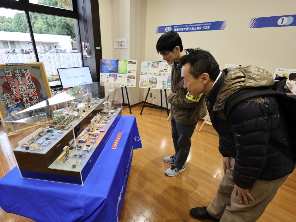 テーブルの上の幅1m強のジオラマを眺めるスタッフ二人