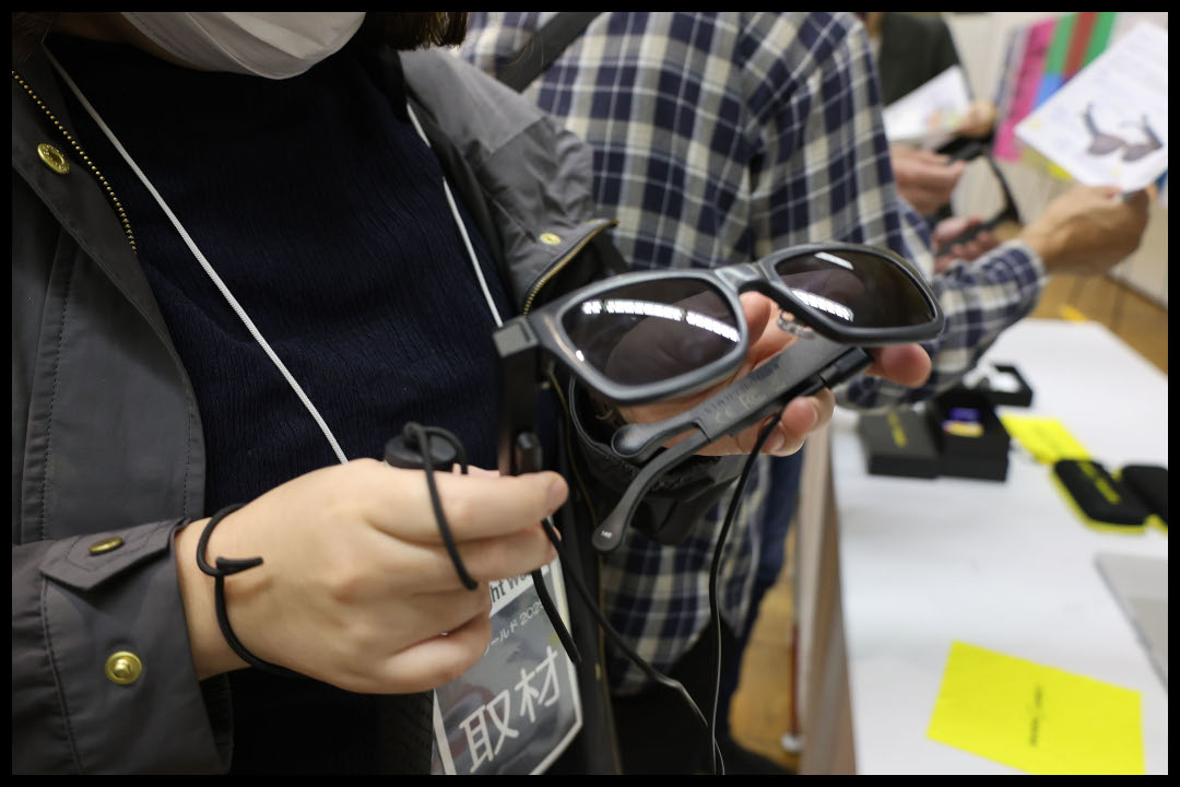 マスクをした人物が、歩行支援やナビゲーション機能を搭載したスマートグラスを手に持っている