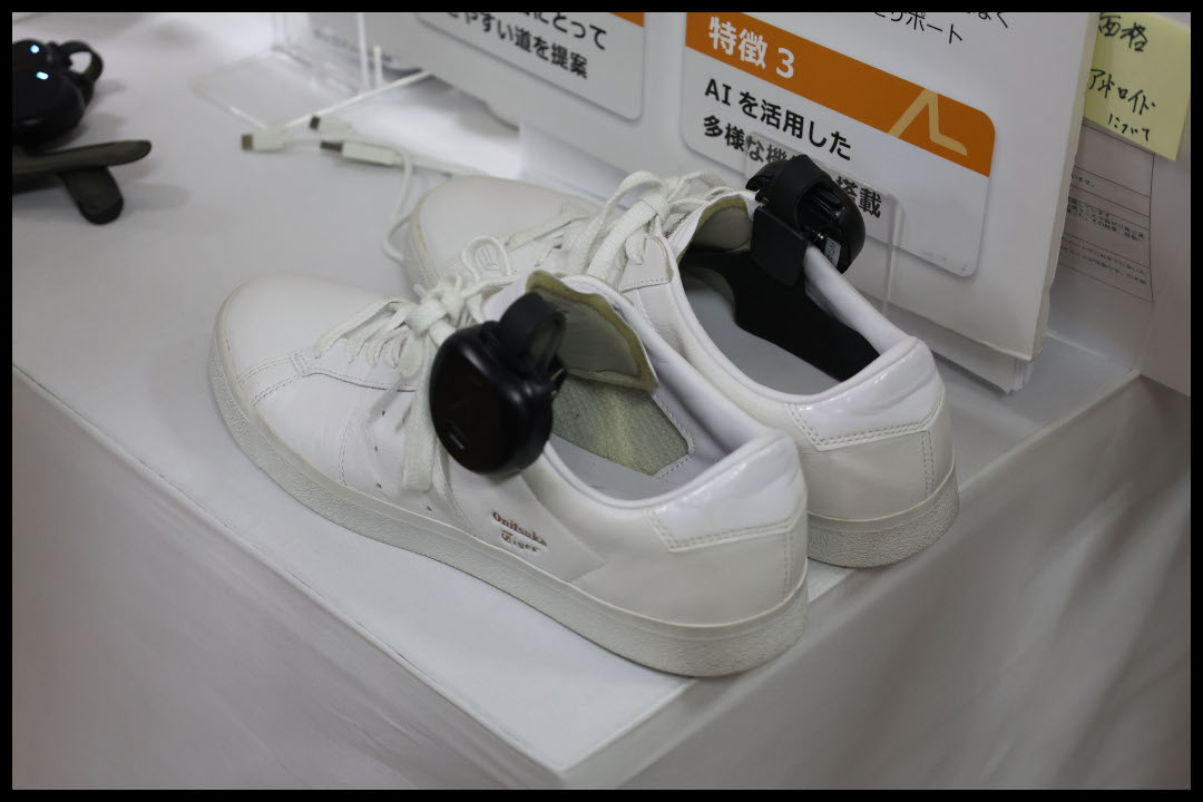 白いスニーカーに装着された、視覚障害者向け歩行ナビゲーションデバイス「あしらせ」の黒い本体