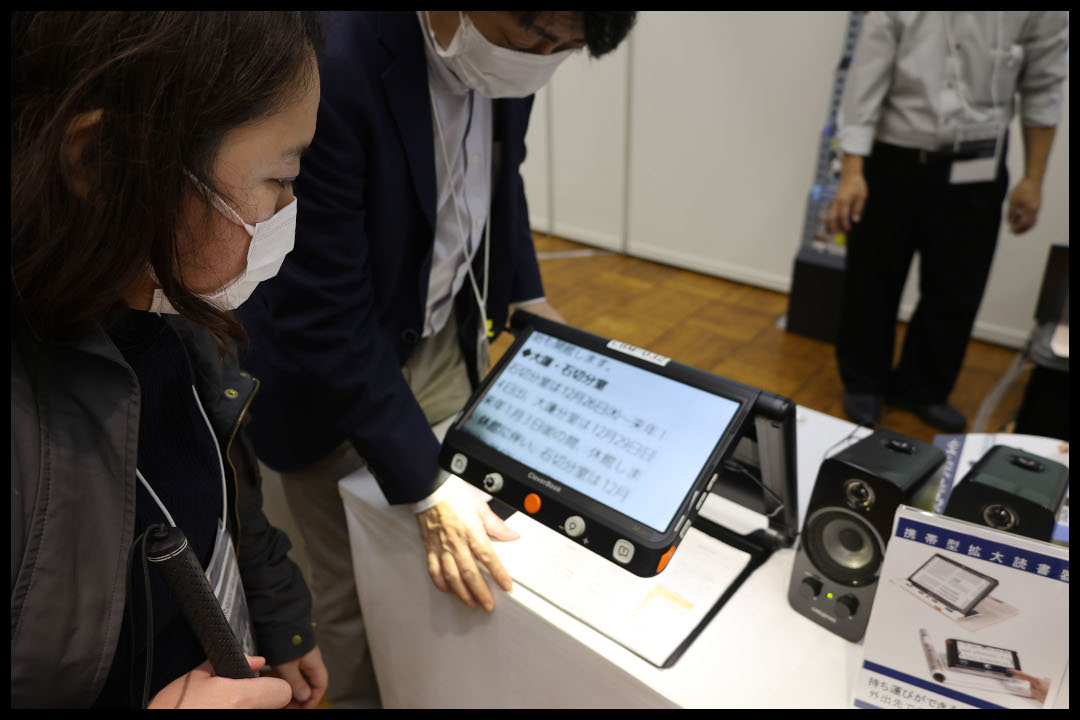 ライターがクローバーブックのデモを見ている様子　タブレットのような画面の下に折りたたみ式のアームとスタンドが付いている