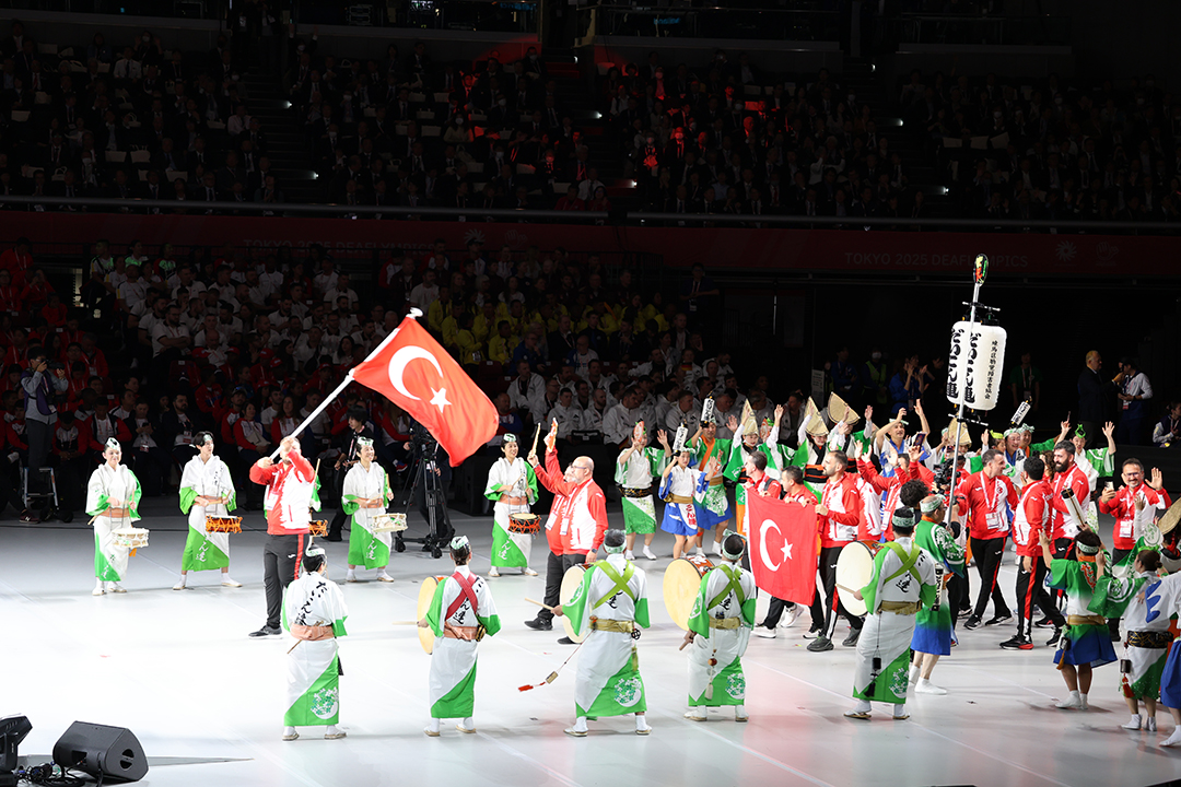 男性が高々と国旗を振っています。上着の色は国旗の赤と白で、ズボンは黒でサイドに赤のストライプがあります。