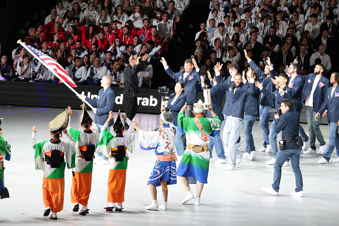 短髪の男性が国旗を振ってます。ユニフォームは紺色の上着でズボンは青系ジーパンです