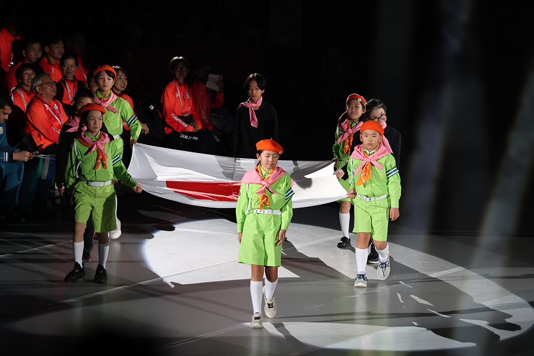 緑の衣装にオレンジ色の帽子をかぶった7人の子供たちが国旗を持ってきました