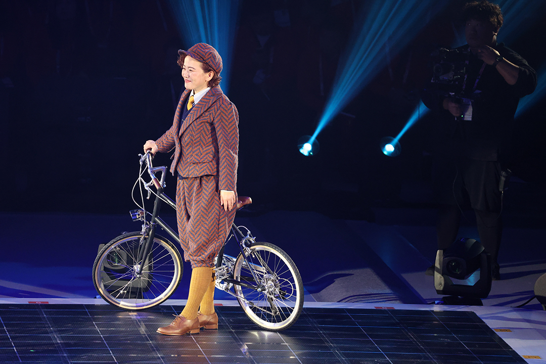 自転車の横に立つ茶系の衣装の大橋氏