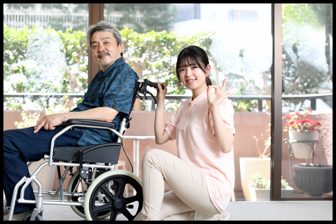 車いすの男性と、その後ろでしゃがんでOKのハンドサインをする女性