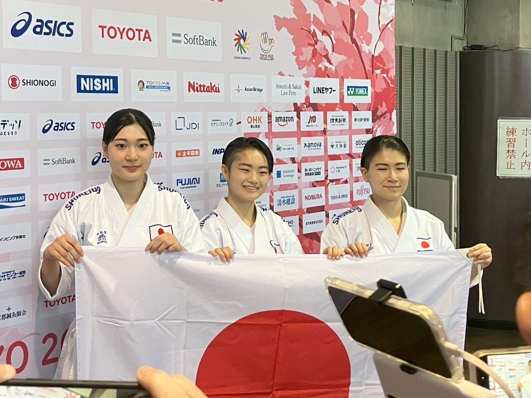 記者会見ボードの前で日の丸を掲げる金子選手、森選手、湯澤選手