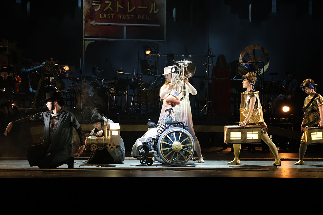 管楽器を持った白い帽子と衣装の男を中心に金色の衣装の男が並びます