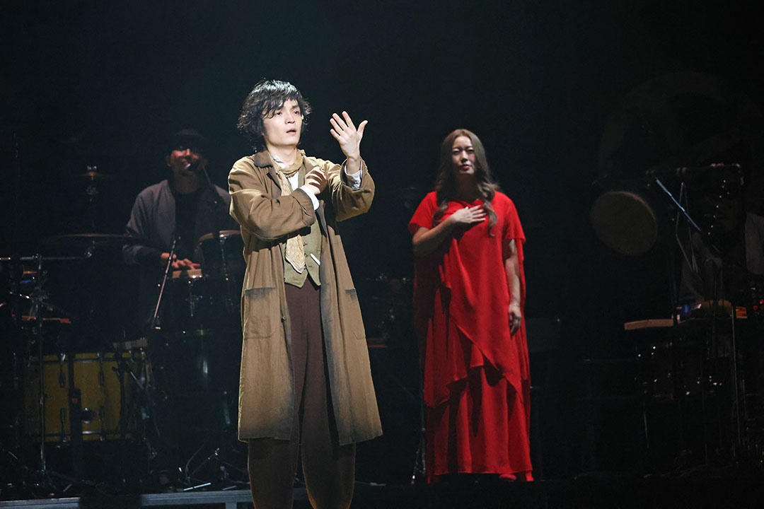 自分のてのひらを見つめる男性と赤い衣装の女神がいます