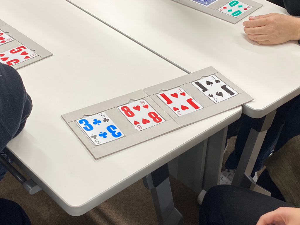 文字が大きいトランプ4枚が手作りのボードに収まっている様子。点字を読む際にカードがずれないように工夫されている